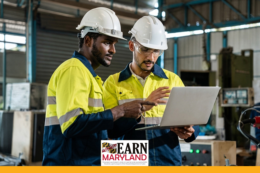 Two mechanical technicians in hard hats and safety gear reviewing a laptop together in an industrial warehouse