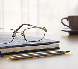 A workspace featuring a journal and glasses, representing professional development, research, and faculty information resources.